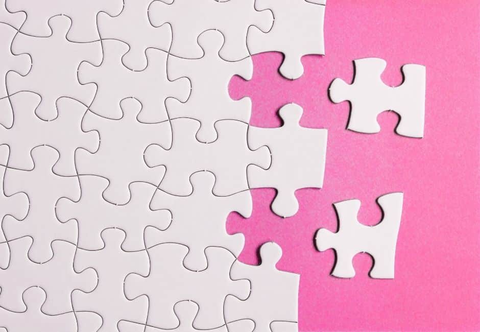 White puzzle pieces, mostly made up with two loose, against a bright pink background