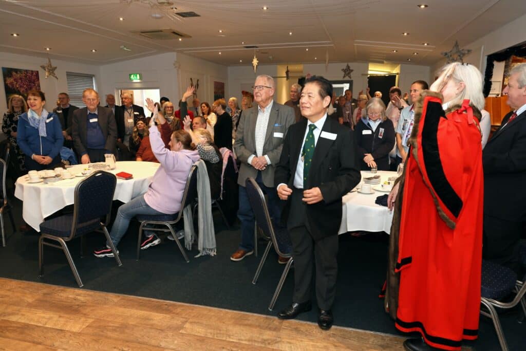 Volunteer awards attendees stand, looking towards stage, including Surrey Heath mayor in red and black robe.